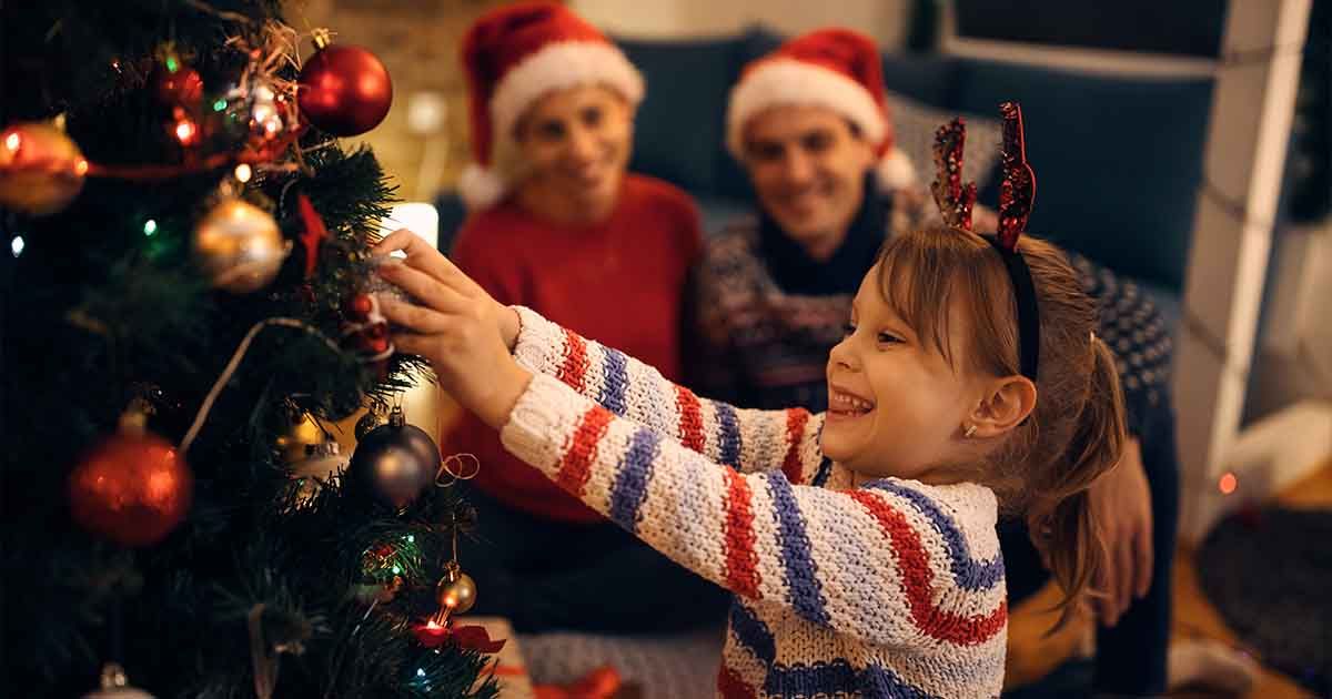 Child decorating tree with parents watching in background.