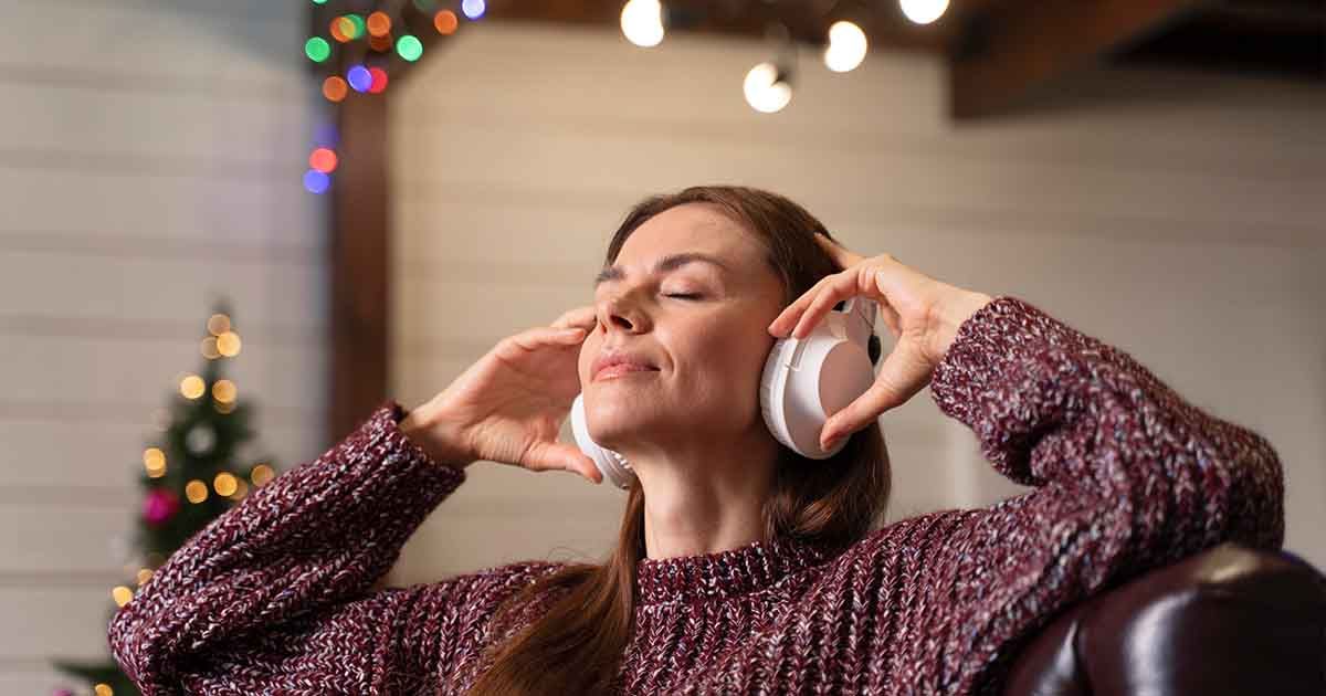 Woman relaxing on couch with headphones on, festive background.
