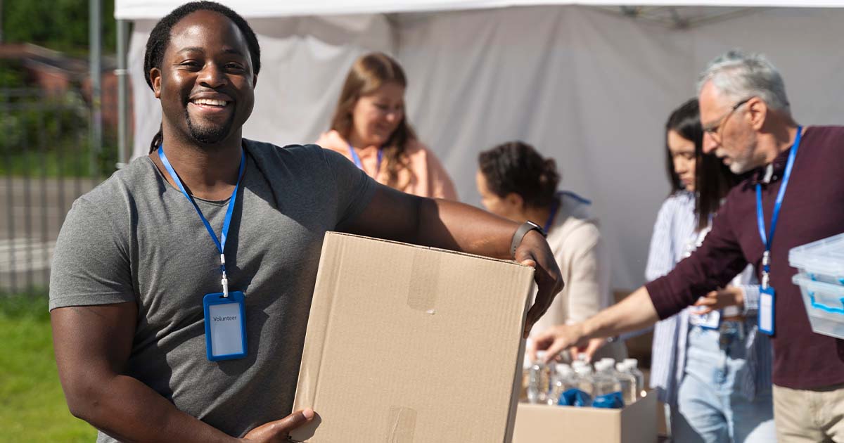 Shelter volunteer holding a cardboard box with other volunteers in the background.