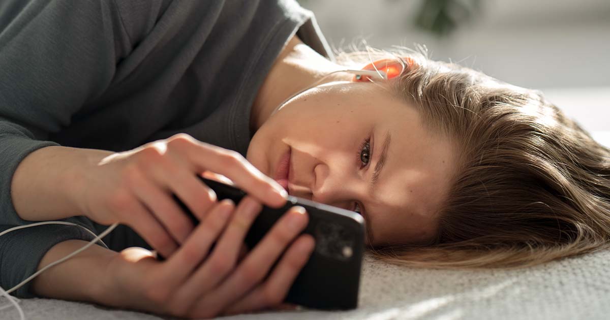 Woman lying on the floor while looking at cell phone.