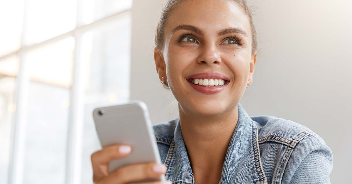 Woman smiling while looking up from cell phone.