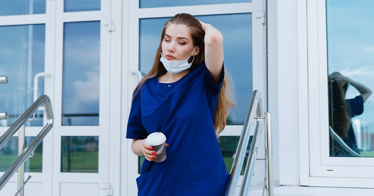 Woman in scrubs leaving building, holding coffee.