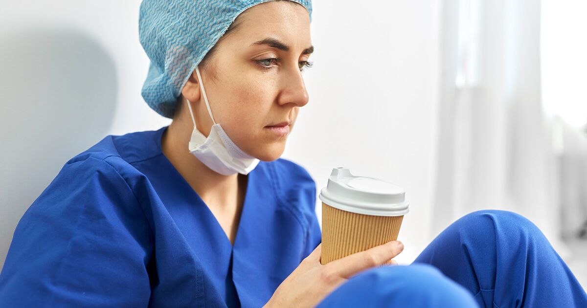 Female nurse sitting on ground, looking tired, holding coffee