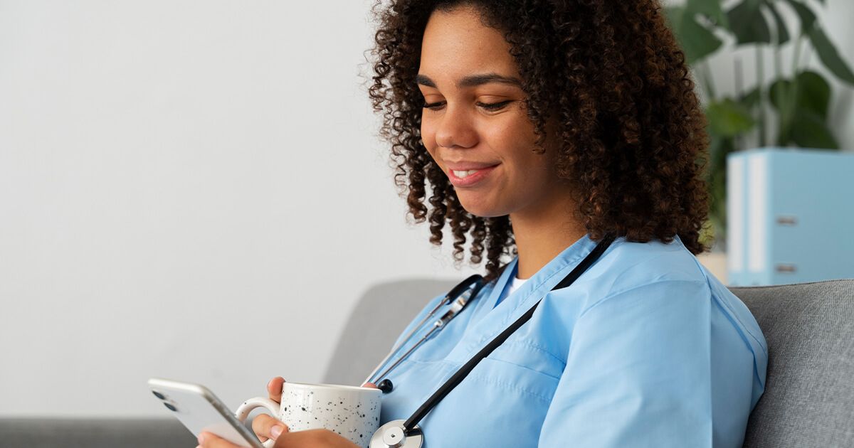 Female nurse sitting with coffee while smiling on phone.
